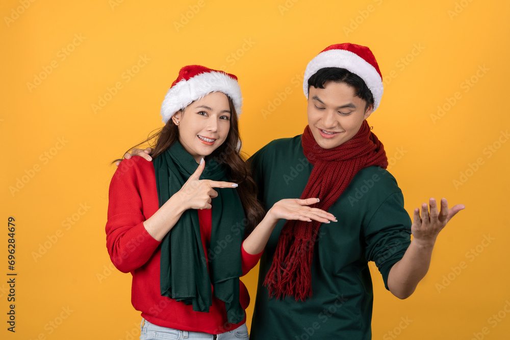 Smiling surprised Asian couple in colorful red and green Christmas clothes on yellow isolated background Smiling surprised Asian couple in colorful red and green Christmas clothes on yellow isolated background