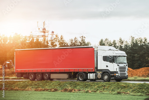 A red truck transports goods across a picturesque landscape illuminated by the golden hue of the setting sun. Truck transportation.