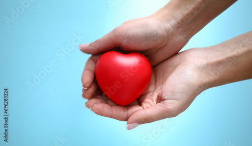 Woman hand hold red toy heart in hand against blue background closeup. Charity people concept