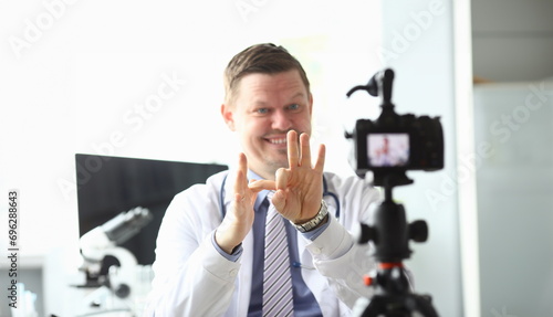 Focus on male hands of handsome doctor showing funny jokes with gestures by hands. Smiling blogger recording popular video content to camera. Blogging concept photo