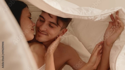 Romantic moment as a sweet couple shares a tender kiss and cuddles under a warm blanket in bed