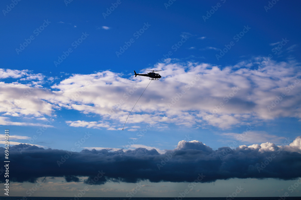Fototapeta premium Silhouette of a helicopter flying over the sea with dramatic clouds