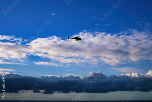 Silhouette of a helicopter flying over the sea with dramatic clouds