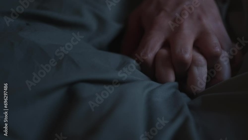Dark slow mo shot of a sign of love. Two hands come together on the bed sheets and they huddle together. Intercourse between a man and a woman. Close shot of hands photo
