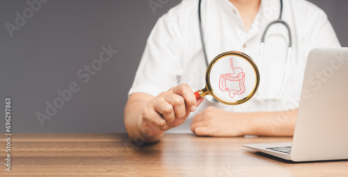 Doctor holds a magnifying glass with an intestine symbol while sitting at a desk in the hospital. photo