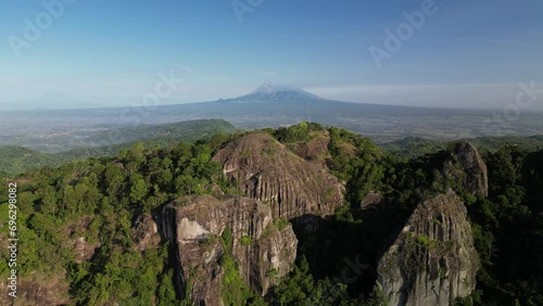 Mount Merapi seen afar from the peak of the Nglanggeran Ancient Volcano, Gunungkidul, Yogyakarta with clear blue sky background. The volcano is visible from behind the rocky mountains and forest. photo