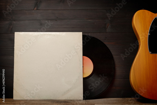 Blank cardboard record sleeve and a guitar on wood wall