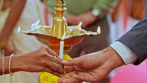 Closeup of male and female hands lighting diya oil lamp with a lit candle at event photo