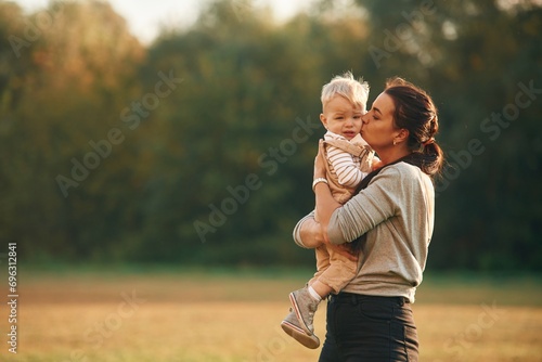 Holding kid in hands. Mother is with her little baby son are outdoors together photo