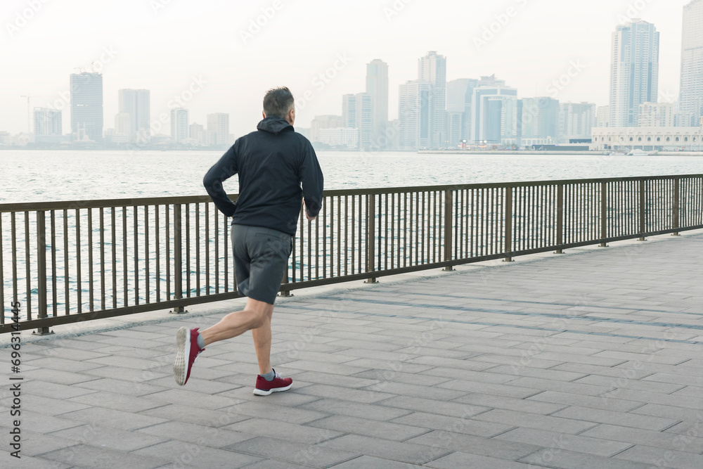 sportsman man he in sports clothes training run jogging at sunrise. senior man running on pier in front of city skyline. healthy lifestyle.