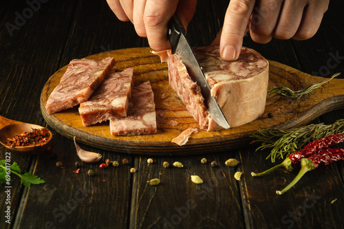 Slicing headcheese on a kitchen board before setting the holiday table. Knife in a man hand while cutting brawn