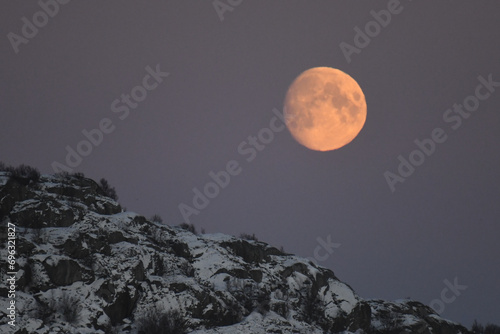 A near full moon is slowly creeping behind a mountain along the norwegian coast on an early winter morning near the town of Bodo. photo
