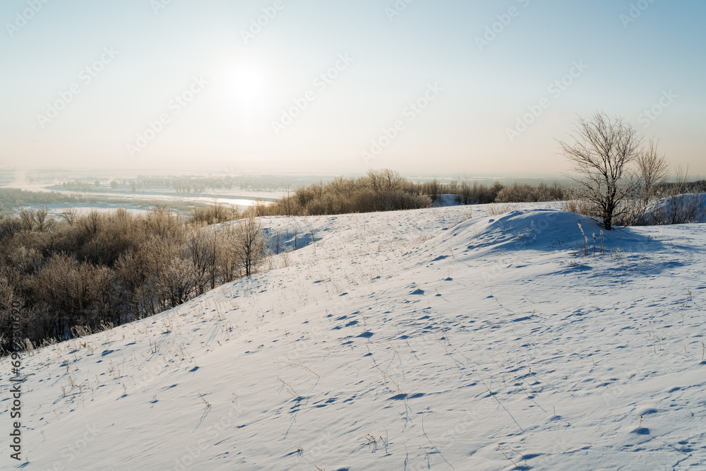Winter landscape on a frosty day, mountain slope covered with snow, setting sun over the horizon, mountain ranges.