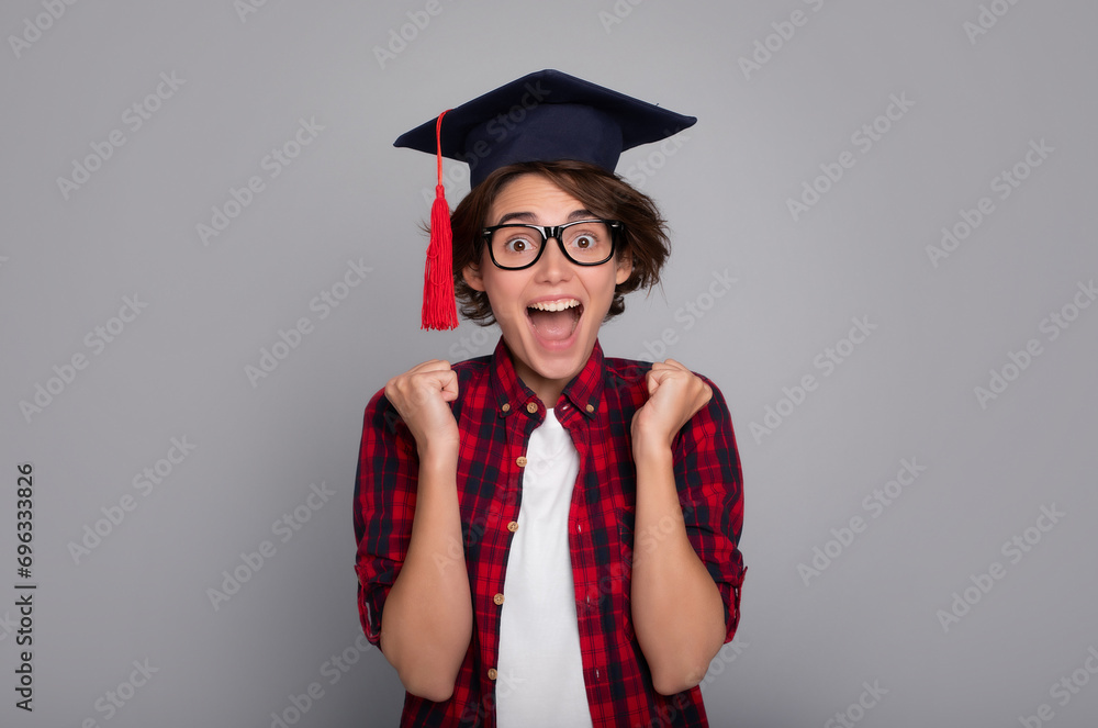 I received a diploma! Portrait of a beautiful, young and surprised graduate in a master's cap with raised fists isolated on gray wall. University, study, education, college, knowledge, graduation. I received a diploma! Portrait of a beautiful, young and surprised graduate in a master's cap with raised fists isolated on gray wall. University, study, education, college, knowledge, graduation.