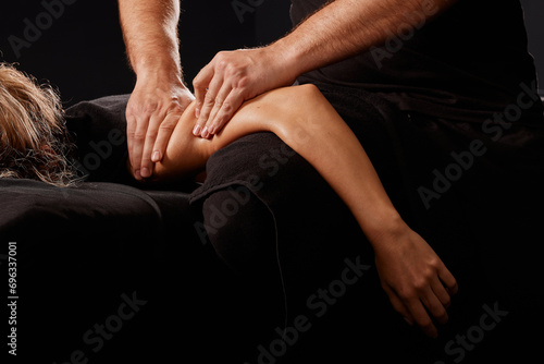 handsome male masseur giving massage to girl on black background, concept of therapeutic relaxing massage photo