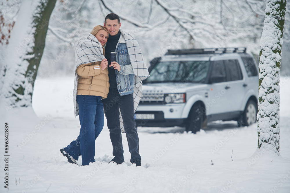 Embracing each other. Beautiful couple standing near the car in the winter forest