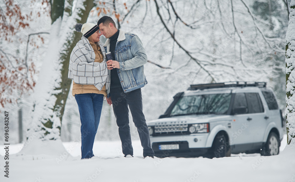 Beautiful couple standing near the car in the winter forest