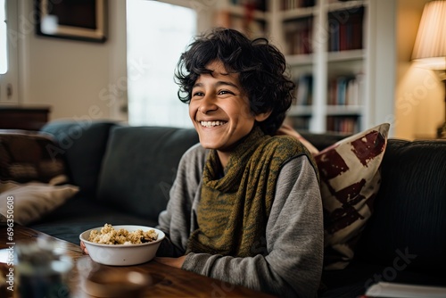 A happy Indian teenager on a sofa, enjoying cereal indoors. photo