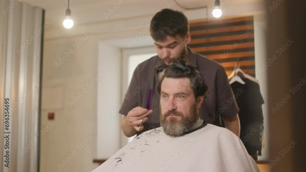 Barber using comb and spraying hair of male client with water while giving haircut in hairdressing salonBarber using comb and spraying hair of male client with water while giving haircut in hairdressi