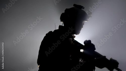 Silhouette of military soldier, warrior puts a clip ammo magazine in a weapon assault rifle carbine. Shadow of mercenary in army camouflage. War concept. Fog smoke in background. Uniform and helmet