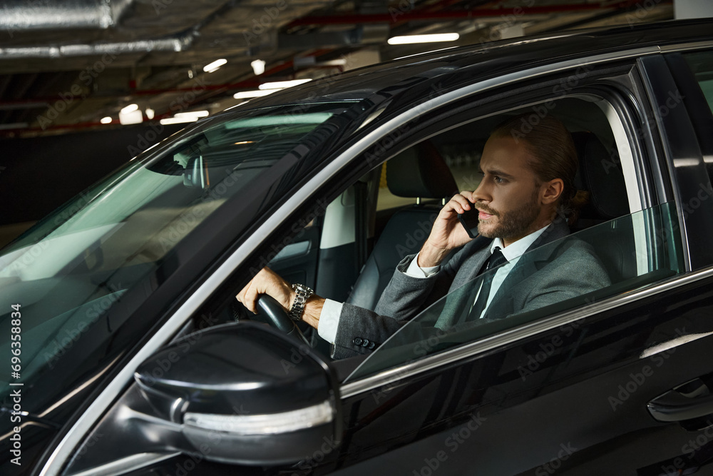 appealing elegant professional in chic suit talking by phone behind steering wheel, business concept