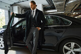 good looking elegant man in smart suit and coat posing next to his car with hand in pocket, business