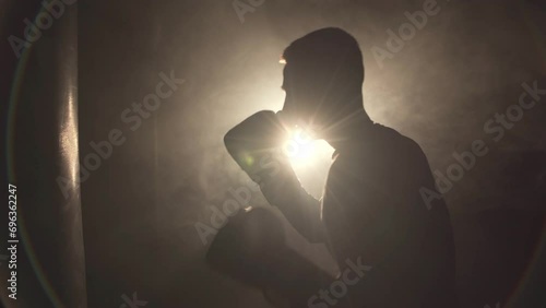 Silhouette of young man doing boxing training at the gym, hitting the punching bag wearing boxing gloves photo
