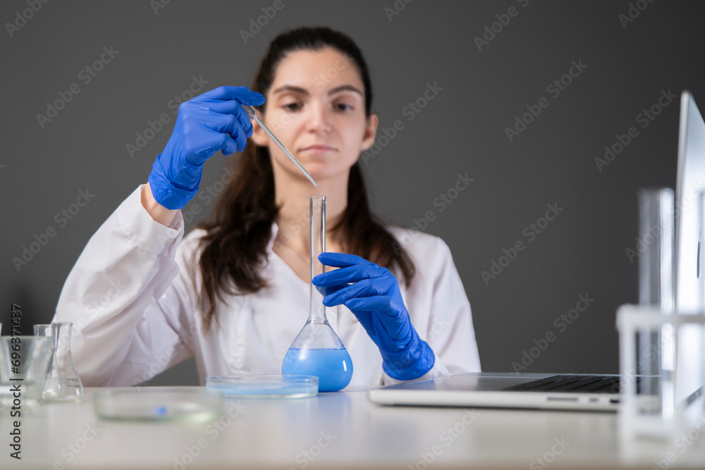female laboratory worker drop some blue liquid from pipette in the glass flask female laboratory worker drop some blue liquid from pipette in the glass flask