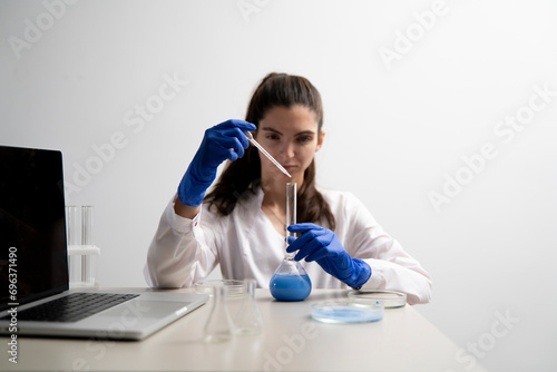 female laboratory worker drop some blue liquid from pipette in the glass flask