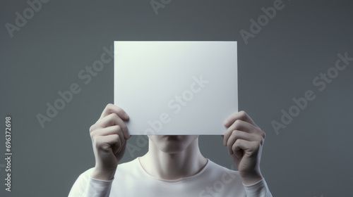 Man hiding his face behind a sheet of paper. Gray background.