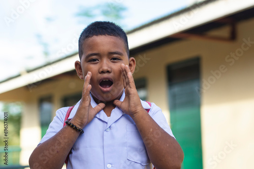 A young rambunctious filipino boy yells outside the classroom school. A rural elementary student wearing his school uniform.