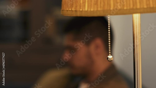 Side stab closeup of blurred bearded man sitting on sofa and turning on floor lamp by pulling chain in modern house photo