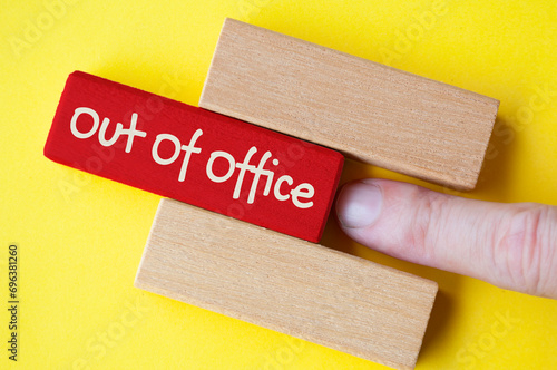 Finger pushing out red wooden block with out of office text on yellow cover background #696381260