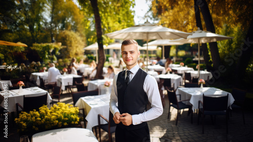 Young cheerful waiter on summer restaurant patio