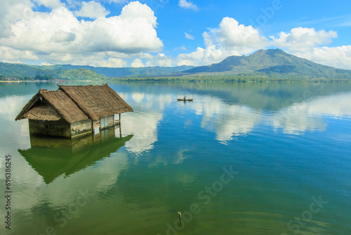 Beautiful Lake Batur landscape overlooking serene and beautiful Mount Batur during blue sky cloudy day with abandoned sub-merge house at foreground. photo