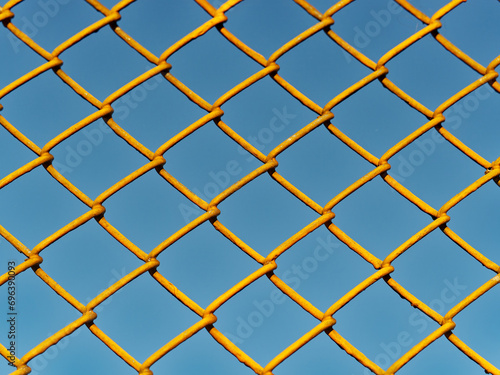 diamond patterned wire mesh blocking our freedom in front of the blue sky on a sunny day
