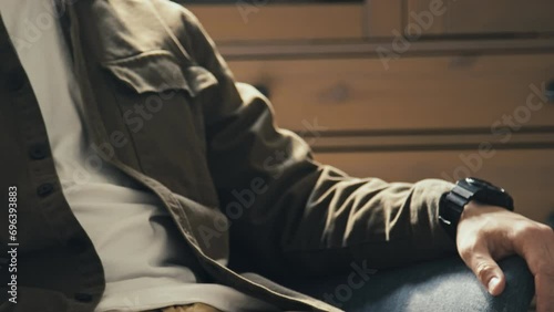 Midsection side stab shot of unrecognizable man using phone sitting on sofa or armchair in living room and then pressing lock button