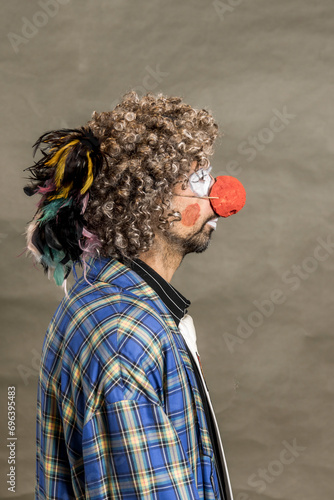 A cheerful curly-haired clown grimaces. A close-up portrait in profile against a background of beige wings. The clown in the parrot tie