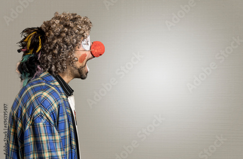 The cheerful curly-haired clown one screams. A close-up portrait in profile against a background of beige wings. The clown in the parrot tie