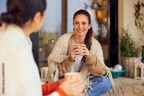 Focus on the smiling brunette woman, sitting with her friend outdoors, during the autumn season, holding a cup of tea.