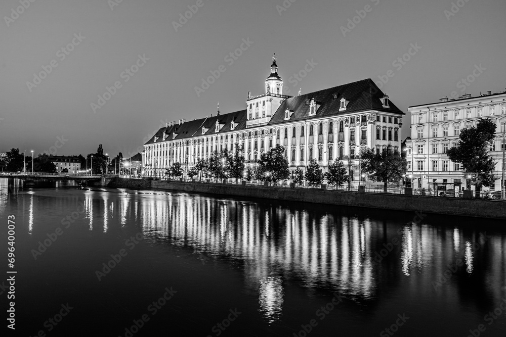 Evening cityscape of the University of Wrocław building illuminated and reflected in the Odra river in Wrocław, Poland in black and white