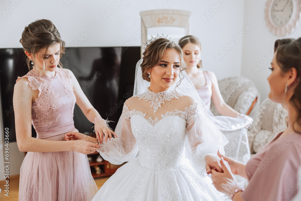 Naklejka premium Morning of the bride. The bride's maid of honor helps the bride lace up her dress, fasten buttons on the dress or sleeves. Girlfriends help the bride fasten her dress