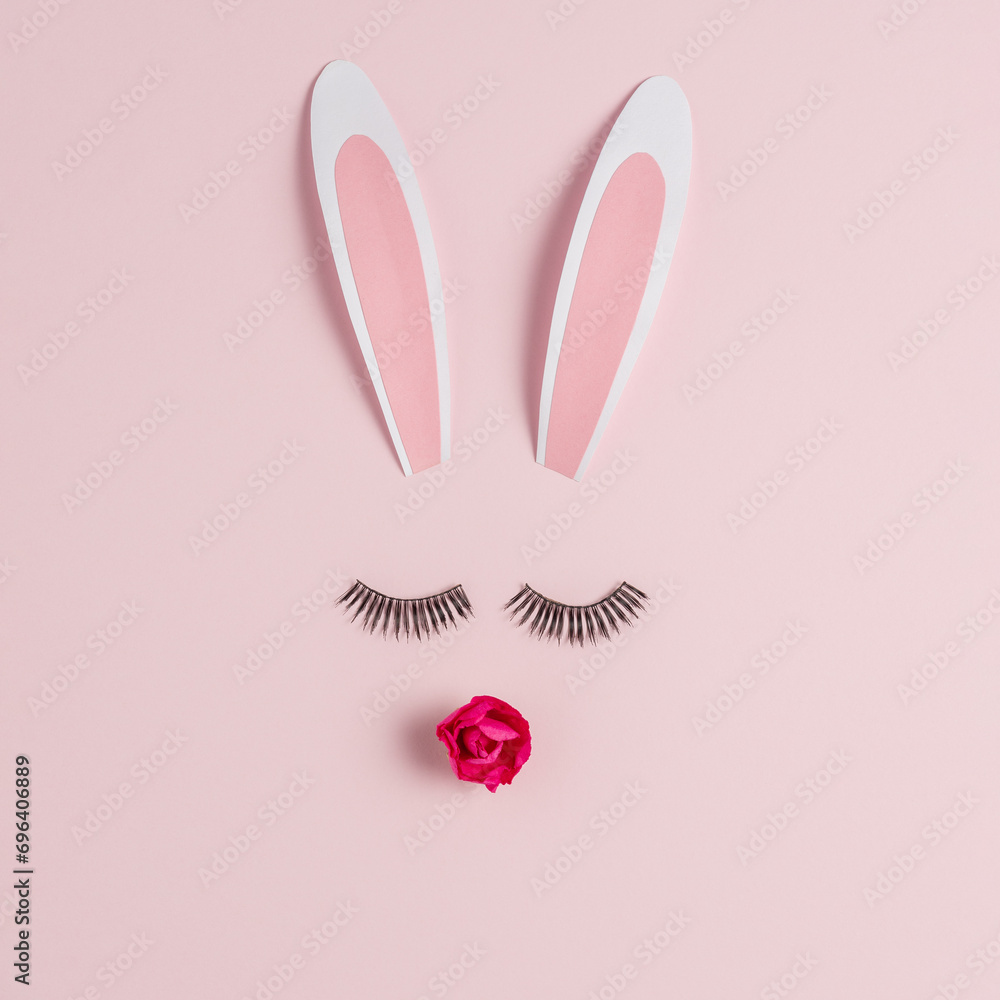 Easter bunny face made of rabbit ears with eyelashes and rose flower on pink background. Happy Easter minimal concept.
