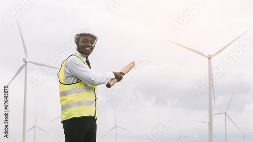 African engineer man stands front the wind turbines generating electricity power station in sunset. .Concept of sustainability development by alternative energy