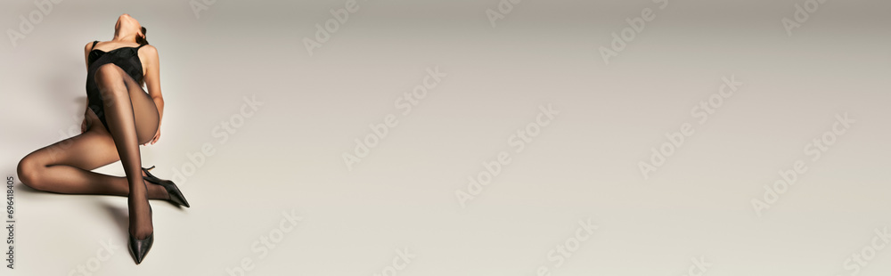 young woman in black bodysuit tights and heel shoes posing on grey background, elegance banner young woman in black bodysuit tights and heel shoes posing on grey background, elegance banner