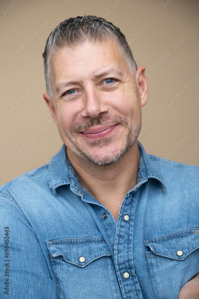 Obraz premium cool man, 46 age, with grey hair, blue jeans, blue shirt, posing in front of brown studio, portrait, concept, business, casual