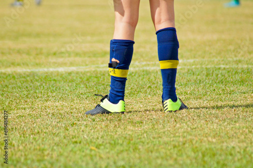 Detail of a young soccer player's legs, on a grassy field, wearing worn-out socks and cleats