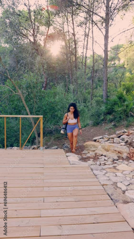 Sporty woman walking through the forest to practice yoga on wooden platform Sporty woman walking through the forest to practice yoga on wooden platform
