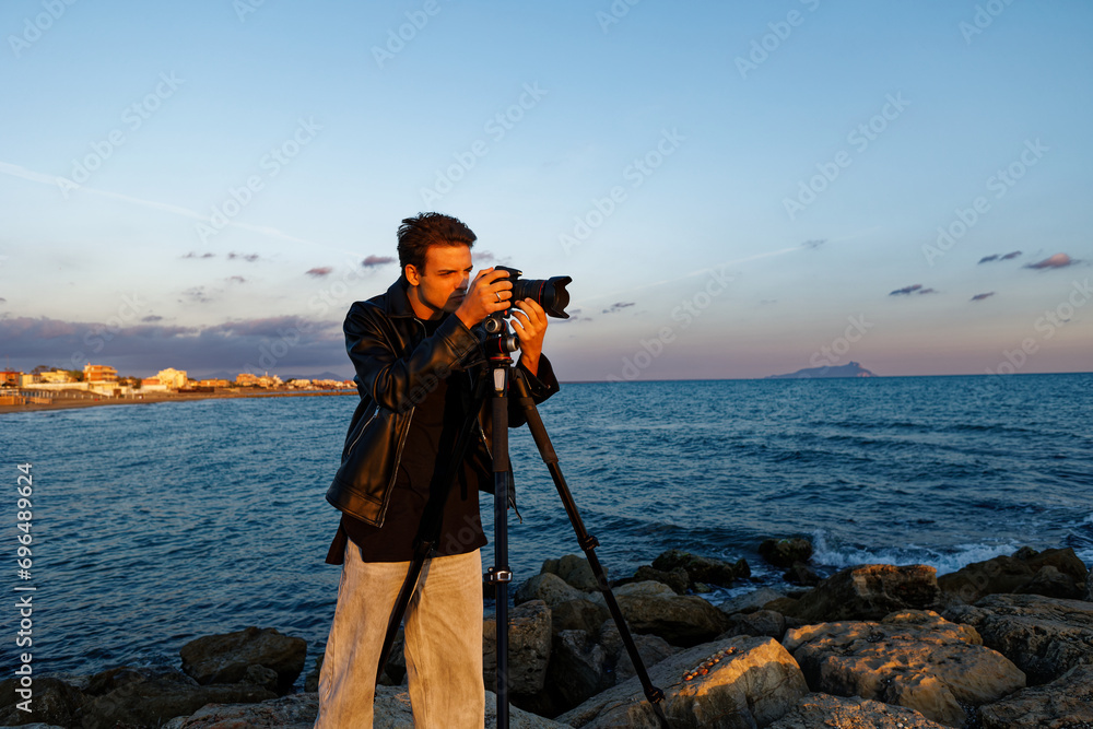 Photographer and travel director on a seaside shooting with models looks into the viewfinder to take the best photo at sunset. Conceptual photo of study on photography. Tourist caucasian outside natur