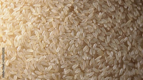 Dry Uncooked Parboiled Rice Background Rotating Right - Top View, Low Key Light. Scattered Raw Long Grain Rice. Asian Cuisine and Culture. Healthy Eating Ingredients. Diet Food photo